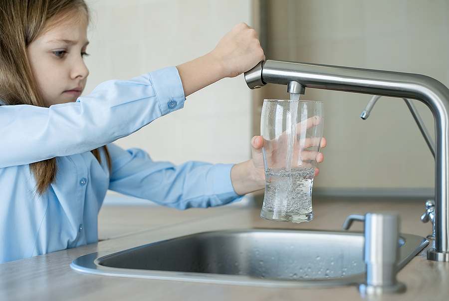 Child pouring glass of water from sink Child pouring glass of water from sink after water filtration system installation